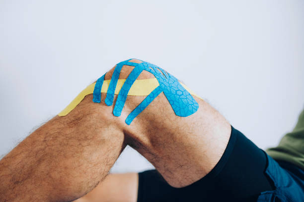 ostéopathie sportif Gros plan du genou d'un athlète masculin avec du ruban kinesio bleu et jaune appliqué dessus